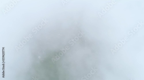 Flying through the foggy clouds in morning. Aerial drone shot flying above a village in the forest. Clouds drift over the beautiful hills and valleys. Foggy sky. Camera look down