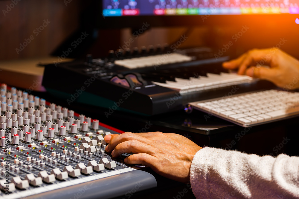Fototapeta premium composer hand adjusting audio level on mixing console while arranging music on computer