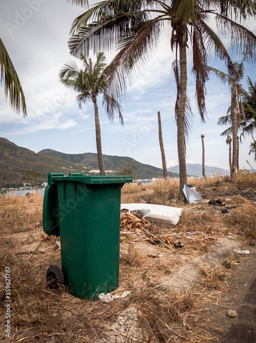 Opened big empty green plastic trash garbage bin in modern comfortable village near sea and palms. Infectious control, garbage disposal, disposal of waste concept. Stories vertical format