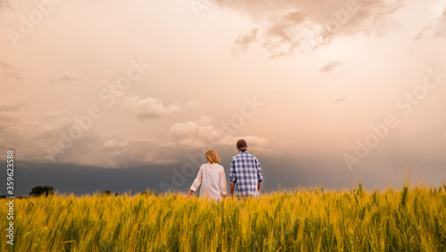 Two farmers in a field of wheat amid dramatic stormy sky