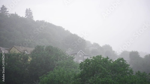 Footage during the storm. The composition includes a few buildings and forest.