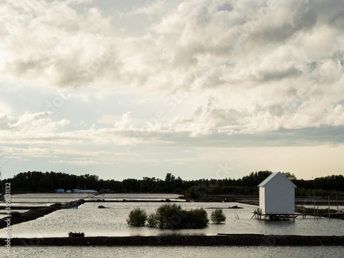 White garden lake house with a white windmill surrounded by ponds with white loudy background. photo