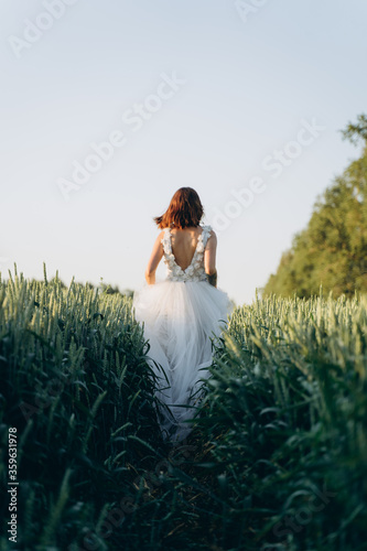 back view of attractive young woman in long white dress standing in the field 