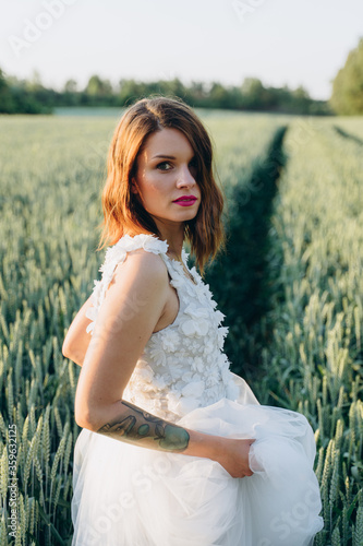 attractive young woman in long white dress standing in the field and looking at camera