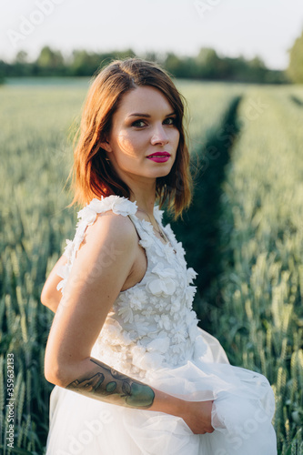 attractive young woman in long white dress standing in the field and looking at camera