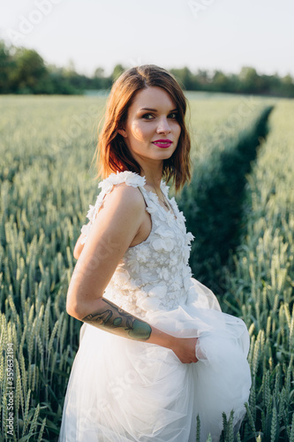 attractive young woman in long white dress standing in the field and looking at camera