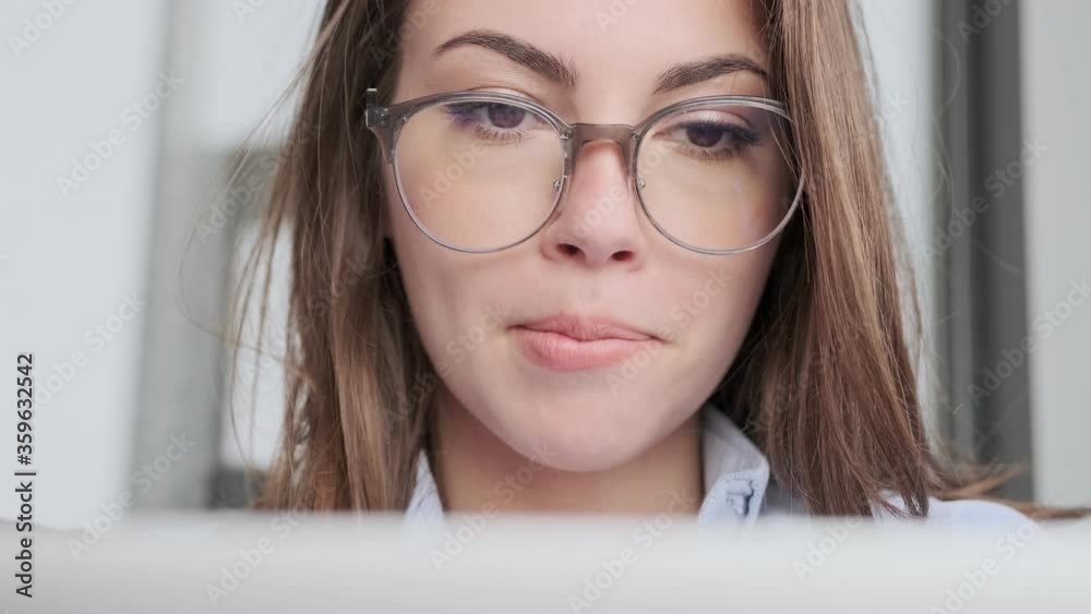 Close up view of Concentrated attractive brunette woman in eyeglasses using laptop computer while sitting on sofa at home Close up view of Concentrated attractive brunette woman in eyeglasses using laptop computer while sitting on sofa at home