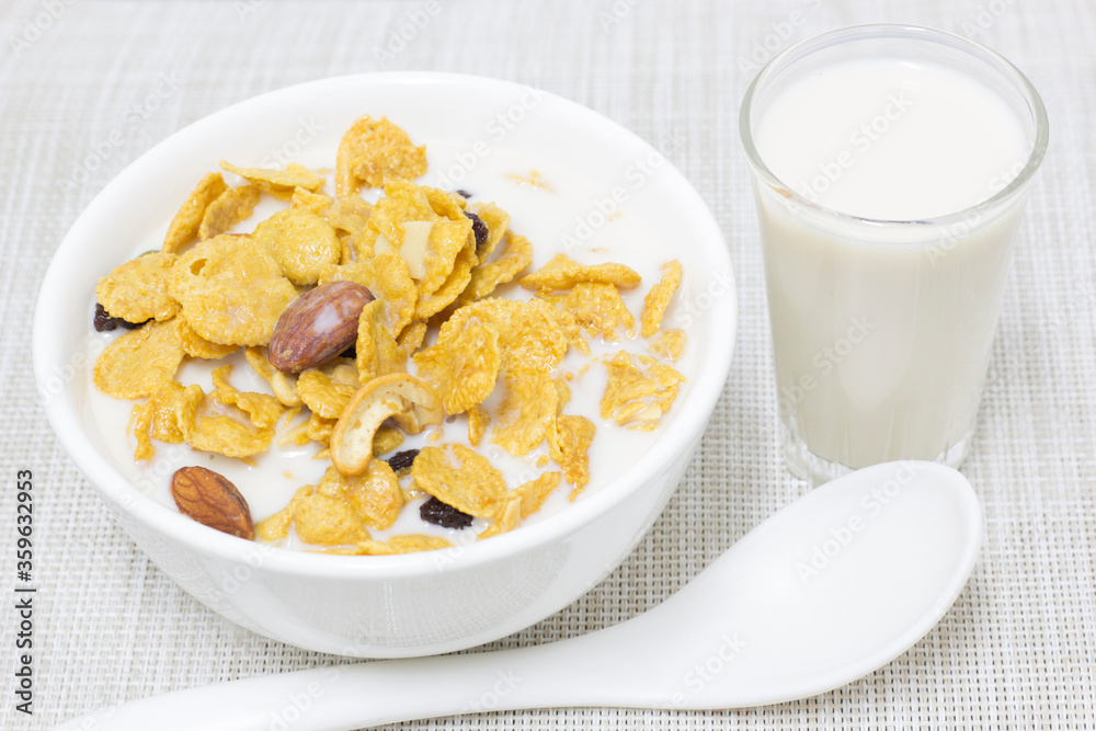Cornflakes, fresh milk in a white cup with a spoon scooping and a glass of fresh milk on the side Cornflakes, fresh milk in a white cup with a spoon scooping and a glass of fresh milk on the side