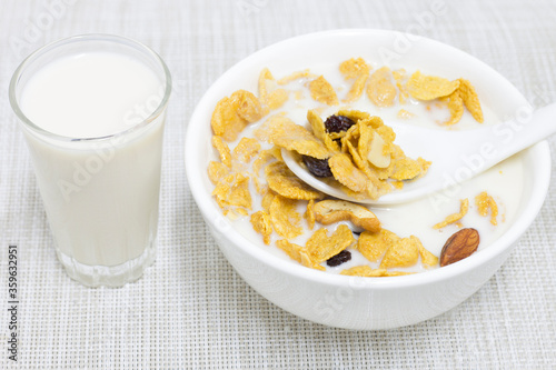 Cornflakes, fresh milk in a white cup with a spoon scooping and a glass of fresh milk on the side