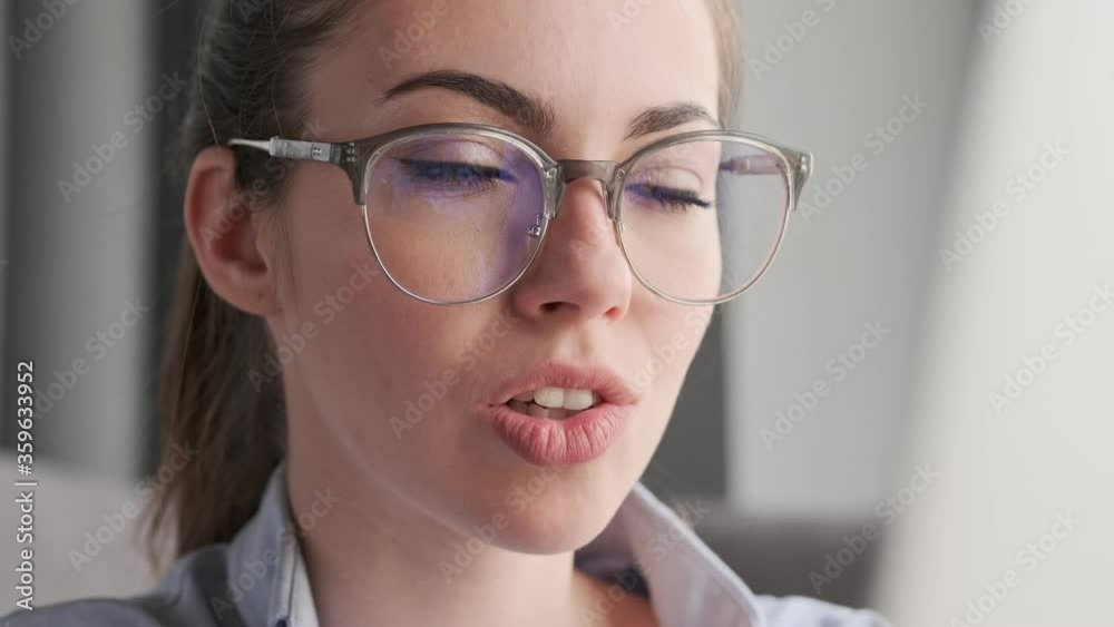Close up view of Smiling attractive brunette woman in eyeglasses using laptop computer at home Close up view of Smiling attractive brunette woman in eyeglasses using laptop computer at home