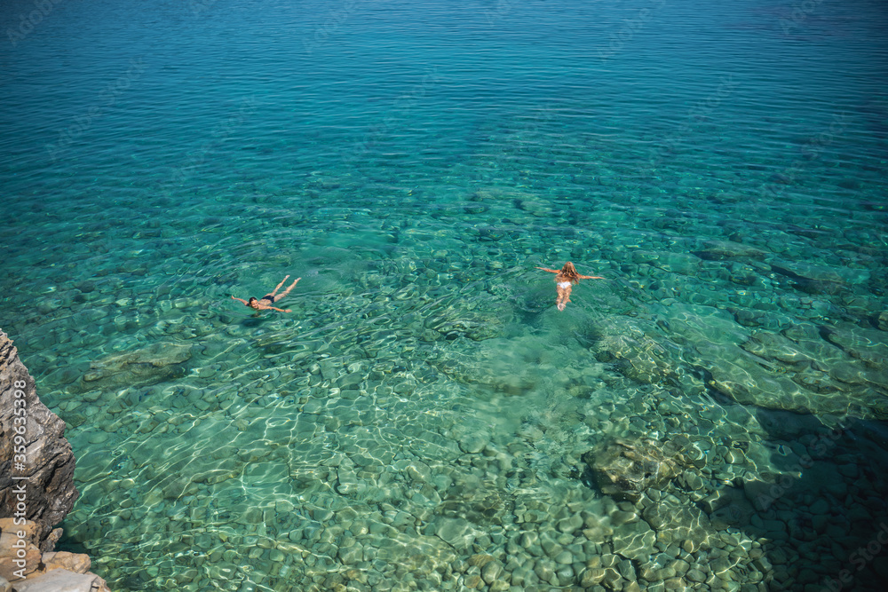 Two women are swimming in the clear sea water, shot from above. Vacation vacation floating and relaxing in nature