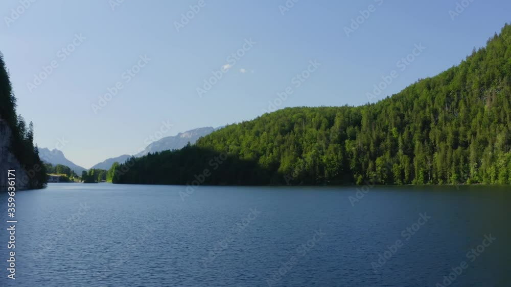 Aerial view moving shot, Scenic view of the lake and tall green trees on the side of the mountains, Blue skies in the background. Aerial view moving shot, Scenic view of the lake and tall green trees on the side of the mountains, Blue skies in the background.