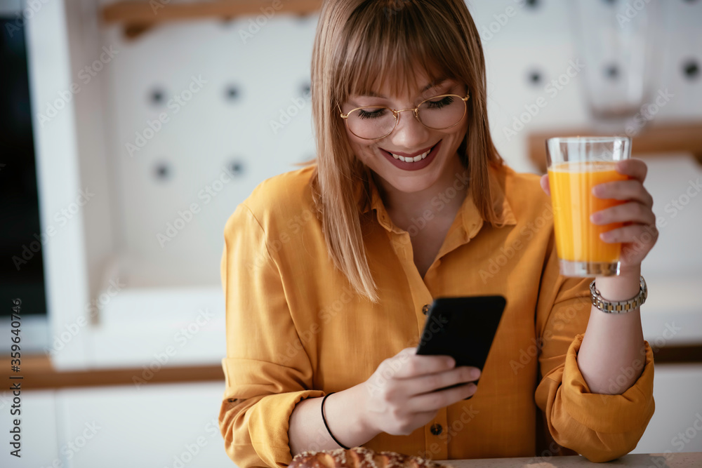Beautiful woman drinking orange juice in the kitchen. Young woman reading the news online. Beautiful woman drinking orange juice in the kitchen. Young woman reading the news online.