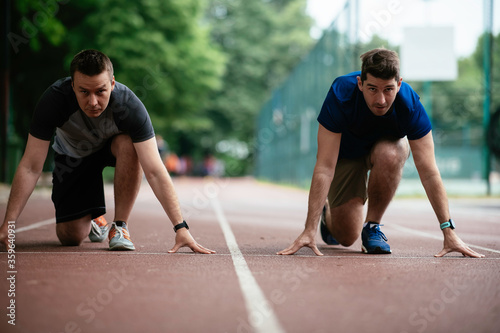 Young men exercising on a race track. Two young friends training outdoors. 
