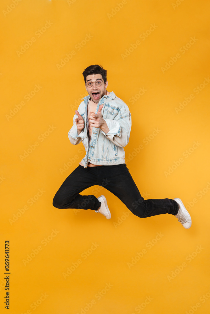 Photo of delighted young man jumping and pointing fingers at camera Photo of delighted young man jumping and pointing fingers at camera