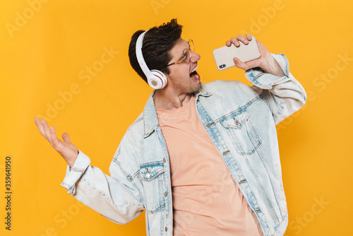 Slika na platnu Photo of ecstatic man using mobile phone and headphones while singing