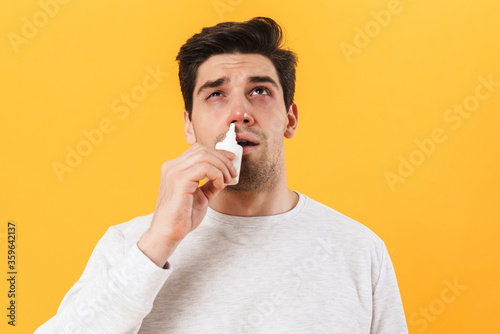 Photo of sick unhappy man with allergy using drops and sneezing