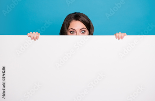 Photo of pretty funny crazy lady hold hands empty advertisement banner peeking eyes hiding face tricky read novelty surprise isolated blue color background