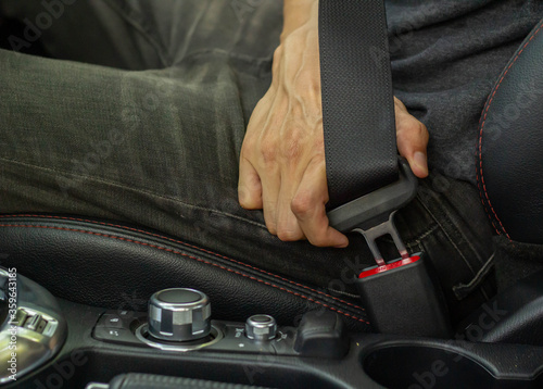 A man's hand is using a car seat belt for safety while driving a private car and preventing danger from a car accident.