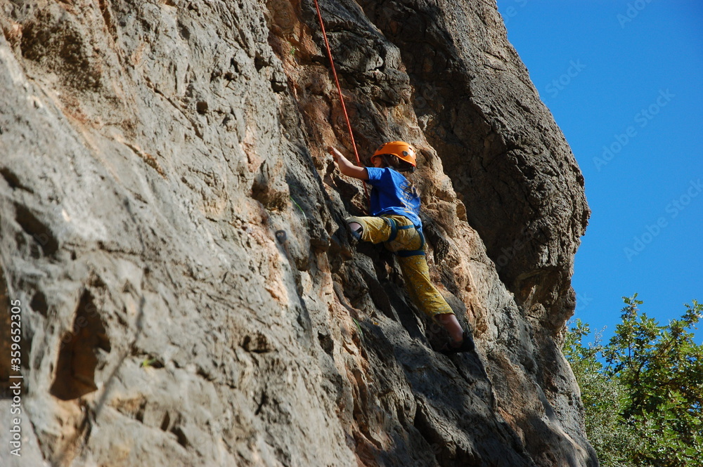 little boy climbs on the rock with rope