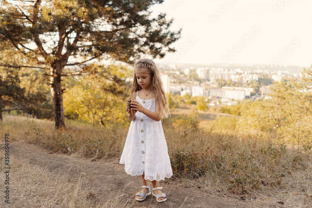 Lovely carefree little girl wearing white clothes enjoy the day and sunshine rays while playing in the nature