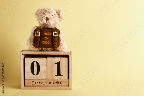 Brown teddy bear with school backpack and decoratibe wooden calendar, yellow background photo