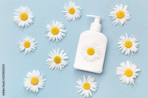 White cosmetic dispenser bottle of cream, gel or lotion with chamomile flowers extract on light blue background. Body skin and health care concept. Top view. Flat lay