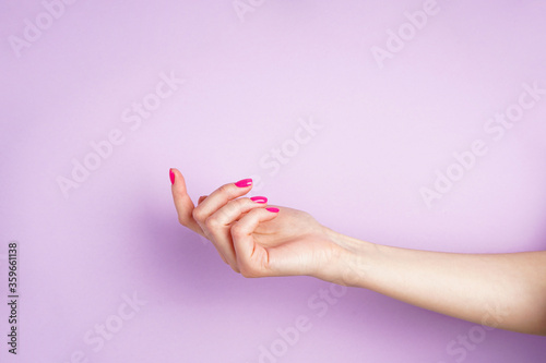 Beautiful hand of a young woman on a purple background. Beautiful manicure with space for text.