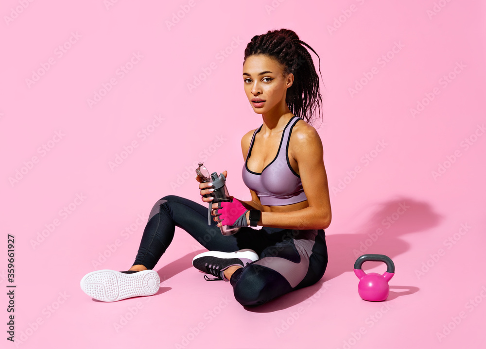 Sporty girl resting after workout with kettlebell. Photo of african american girl in black sportswear on pink background. Strength and motivation Sporty girl resting after workout with kettlebell. Photo of african american girl in black sportswear on pink background. Strength and motivation