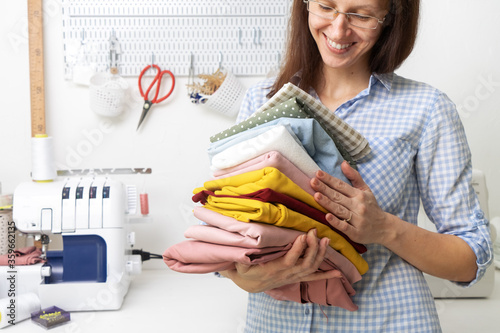 Sewing: the girl smiles and holds in her hands a stack of multi-colored fabrics on the background of a sewing machine. photo