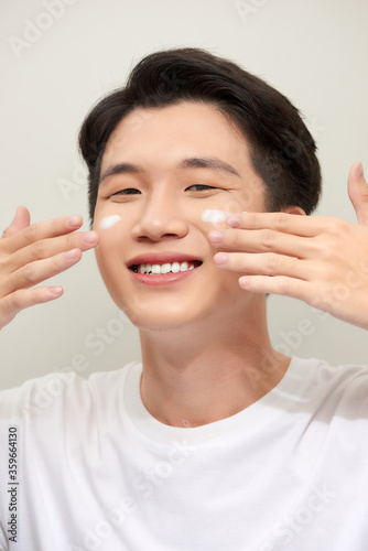 Close-up portrait of a smiling  happy-looking young asian man with moisturizer cream applied on the face.
