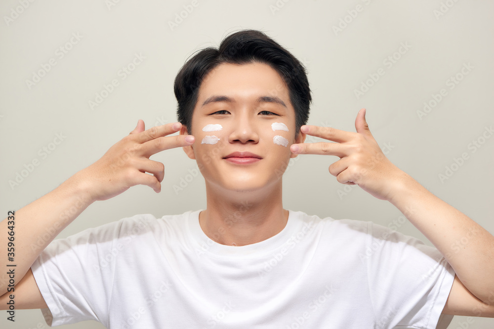 Portrait of a charming handsome young guy has healthy perfect skin, cream on his face, holds moisturizing cream on his face. Portrait of a charming handsome young guy has healthy perfect skin, cream on his face, holds moisturizing cream on his face.