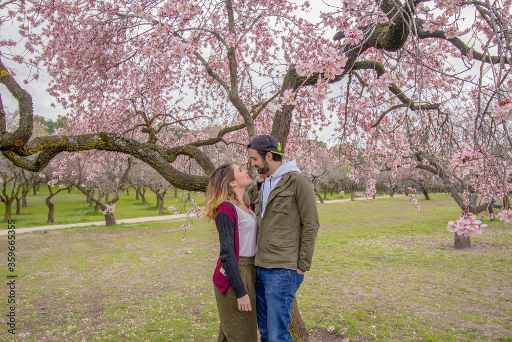 Happy couple with a tree of beautiful flowers on the background in spring season Happy couple with a tree of beautiful flowers on the background in spring season