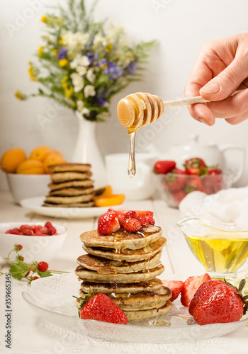 Pancakes with strawberries, delicious breakfast. A woman pours honey on a stack of pancakes. vertical food photo