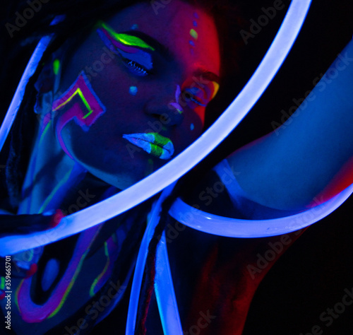 Portrait of a Warror Girl with Glowing Tubes in Neon UF Light. Model Girl with Dreadlocks and Fluorescent Creative Psychedelic MakeUp, Art Design of Female Disco Dancer Model in UV, Colorful Abstract photo