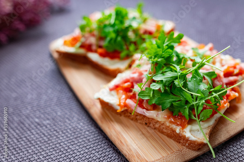 Baked hot sandwiches on white bread with fried vegetables in tomato sauce, Servelat straws, melted cheese and green watercress on a wooden Board