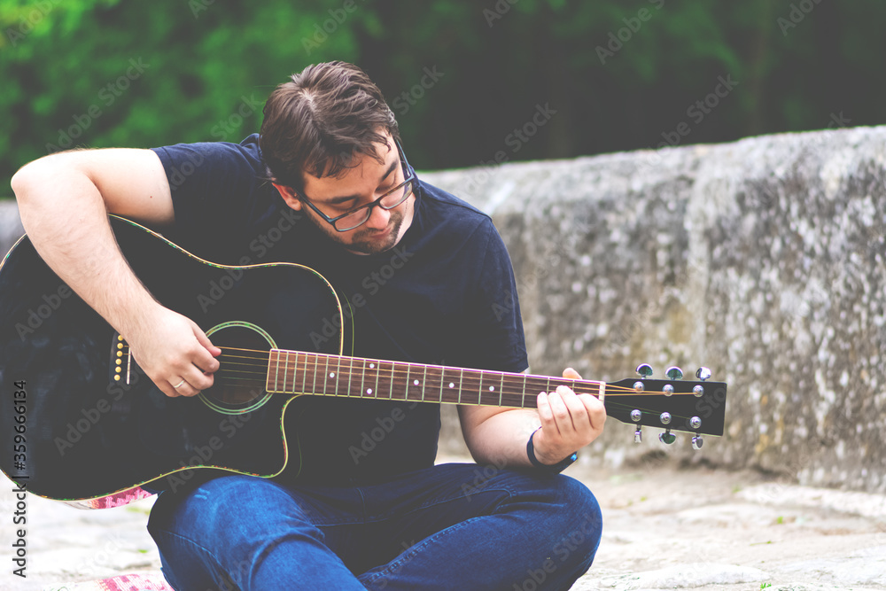 Obraz premium Young man playing guitar sitting on the bridge