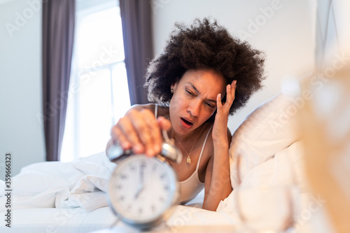 Sleepy young woman stretching hand to ringing alarm to turn it off. Early wake up, not getting enough sleep, getting work concept. waking up with headache