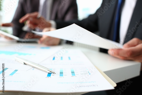 Close up of male workers sitting at the table with financial statistic reports, infographics and silver ball pen