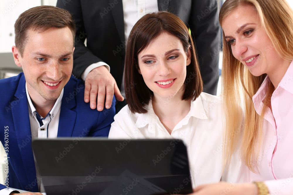 Group of young businesspeople looking at electronic pad PC and smiling while sitting at the table at work Group of young businesspeople looking at electronic pad PC and smiling while sitting at the table at work