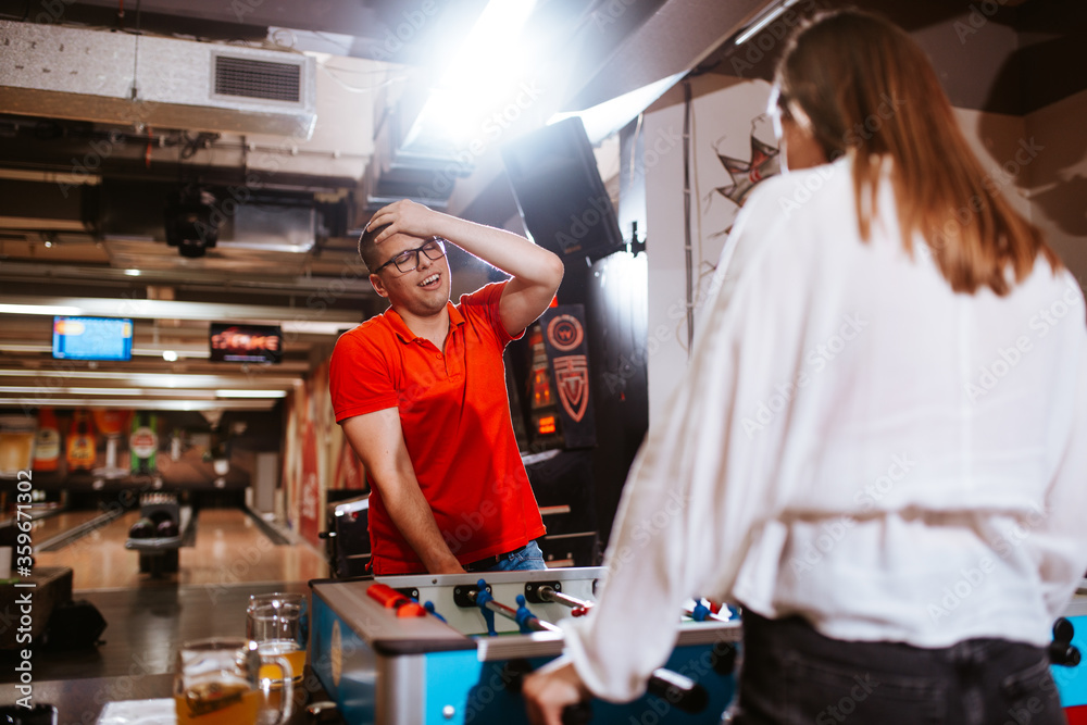 Obraz premium A beautiful caucasian girl and a man with glasses play table football in the playroom. Love and fun time