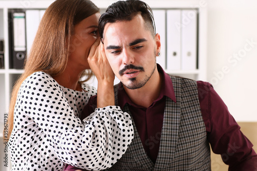 Cheerful female worker telling gossip to male colleague in office