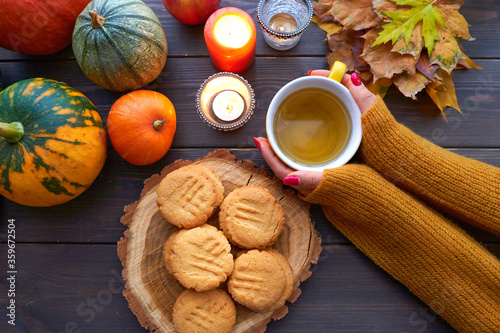 Top view cup of tea with mint in female hand. Homemade peanut cookies  pumpkin and autumn yellow leaves on wooden background.