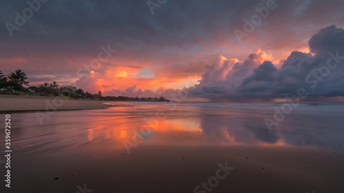 A colourful sunrise with large clouds drifting towards the land