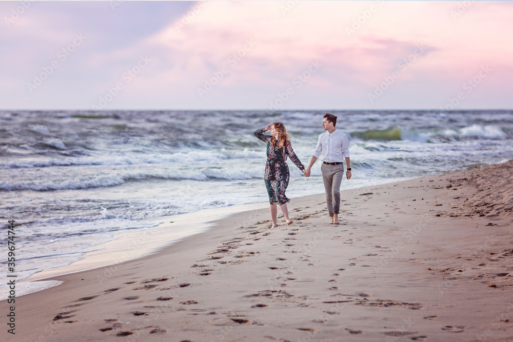 A young couple in love walk along the sea on the sand barefoot holding hands. They look at the sea. Love, trust, always be together concept