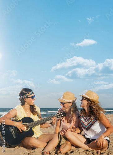 Friends on the beach a sunny summer day. They are laughing sitting on the sand and playing the guitar © Roman