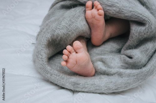 Legs of a young child wrapped in a woolen blanket, close-up on a white bed. The kid sleeps on the sofa, covered with a plaid. Photography, concept.