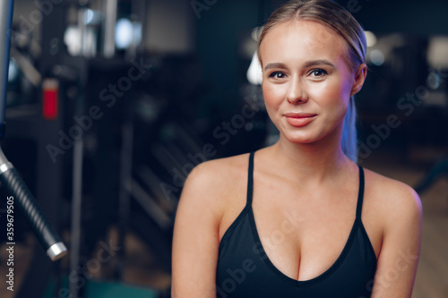 Close up portrait of a young blonde woman in sport bra in a dark gym