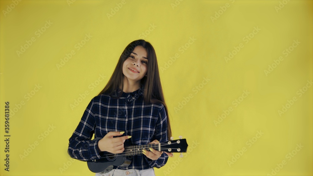 Young girl singing and playing ukulele on yellow Background in Studio Young girl singing and playing ukulele on yellow Background in Studio