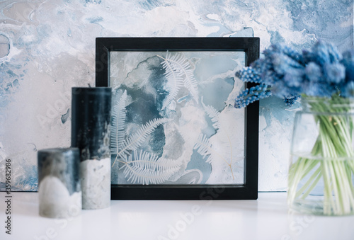 Beautiful hand made black candles and a vase of Muskari flowers behind a glass black frame  still life photo